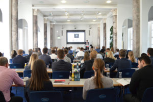 Publikum von hinten, im Hintergrund ein Vortrag 